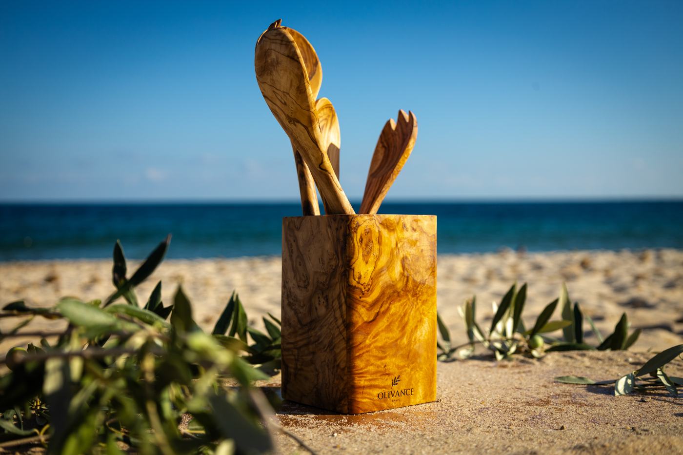 Un pot à ustensiles en bois d’olivier garni de cuillères, face à la mer